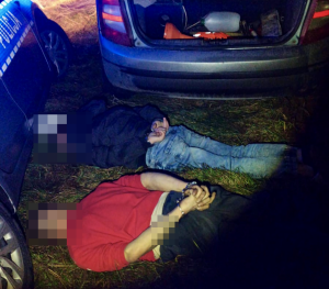 Dwóch mężczyzn zatrzymanych leżą na ziemi obok pojazdów.