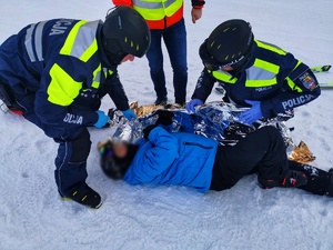 Policjanci udzielają pomocy narciarzowi, który leży na stoku