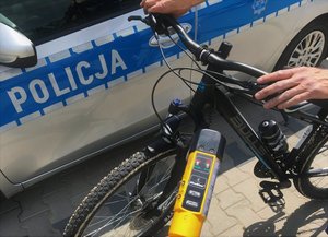 Napis policja na drzwiach radiowozu a w tle rower