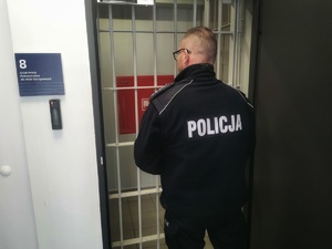 policjant w trakcie czynności służbowych, w tle pomieszczenie dla osób zatrzymanych