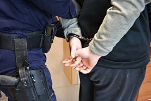 policjant i osoba z założonymi na nadgarstki kajdankami trzymająca ręce za plecami