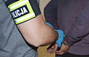 dwóch mężczyzn, jeden ma założone kajdanki na ręce, drugi ma opaskę na ręce z napisem Policja