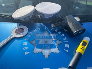 na masce radiowozu leżą: tarcza do zatrzymywania pojazdów , dwie czapki policyjne, urządzenie do pomiaru prędkości i urządzenie do badania trzezwości