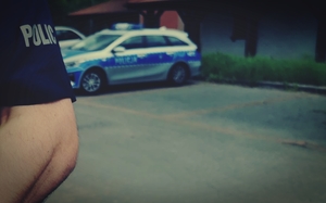 w tle radiowóz i ręka, na koszulce napis policja