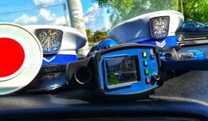 Zdjęcie przedstawia dwie policyjne czapki oraz urządzenie do pomiaru prędkości na drodze