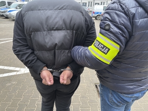 policjant trzyma zatrzymanego w kajdankach na ręce z tyłu