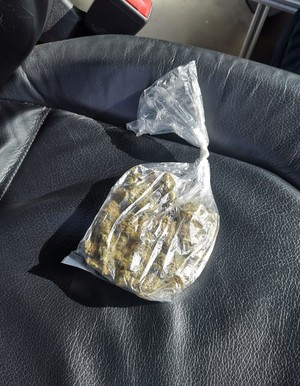torebka foliowa z marihuaną oraz policjantów w żółtych kamizelkach z napisem POLICJA z zatrzymanym.
