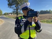 policjant trzymający przy twarzy urządzenie do mierzenia prędkości