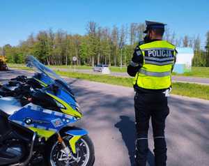 policjant w odblaskowej kamizelce z napisem policja stojący przy motocyklu