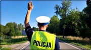 policjant stojący tyłem w kamizelce odblaskowej koloru zielonego z napisem policja, z lewą ręką podniesioną do góry