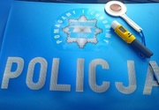 na tle niebieskim z napisem policja leży urządzenie do mierzenia zawartości alkoholu w organizmie oraz przyrząd do zatrzymywania samochodów