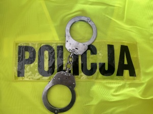 kajdanki na żółtej kamizelce z napisem policja