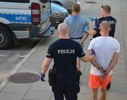 dwóch mężczyzn widzianych od tyłu w kajdankach na nadgarstkach prowadzonych przez dwóch policjantów