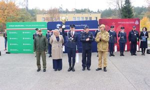 pięć osób stojących obok siebie, w tym dwie ubrane w mundury policyjne, w tle za tymi osobami także widać policjantów stojących obok siebie