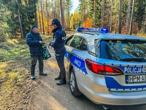 radiowóz a przy nim stojąca policjantka w mundurze oraz mężczyzna