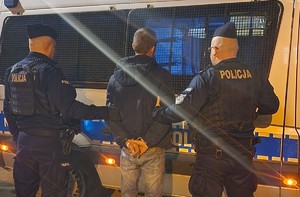 zatrzymany poszukiwany z policjantami którzy stoją przy radiowozie