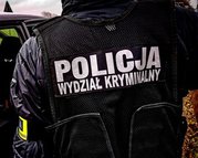 policjant stojący tyłem, na czarnej kamizelce napis policja wydział kryminalny białymi literami