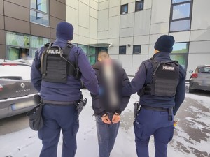 zatrzymany z kajdankami na rekach trzymanych z tyłu, prowadzony przez dwóch policjantów