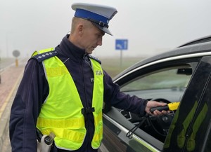 policjant stoi przy pojeździe i bada trzeźwość alkomatem
