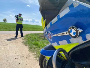 przód motocykla policyjnego i stojący przy drodze policjant z urządzeniem do mierzenia prędkości