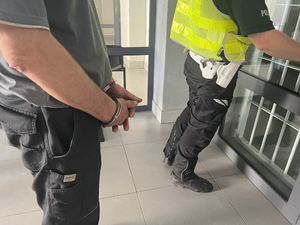 policjant stojący przy kracie a za nim osoba w kajdankach