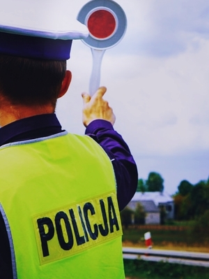 policjant ruchu drogowego widziany tyłem w ręku trzyma urządzenie do zatrzymywania pojazdów