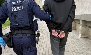 policjant prowadzący męzczyzne w kajdankach na rekach trzymanych z tyłu