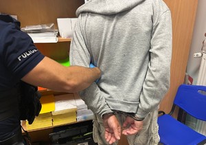 zatrzymany sprawca kradzieży w kajdankach na rękach trzymanych z tyłu