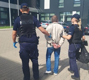 zatrzymany poszukiwany w kajdankach na rękach trzymanych z tyłu prowadzony przez policjantów
