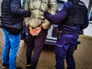 dwóch policjantów prowadzących mężczyznę w kajdanakch
