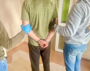 mężczyzna w kajdankach stojący pomiędzy dwoma policjantami po cywilnemu