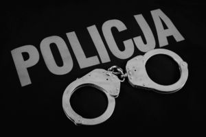 na czarnym tle biały napis policja i leżące kajdanki