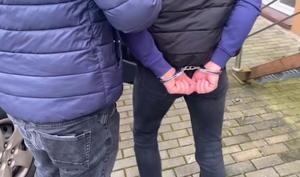 mężczyzna w kajdankach stojący tyłem a obok policjant