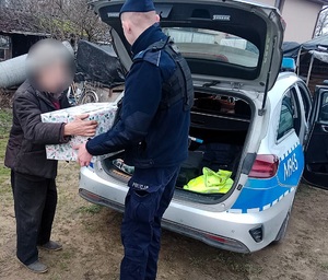 policjant przekazuje pudełko dla mężczyzny w tle radiowóz