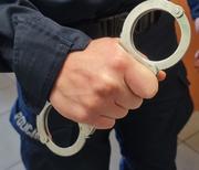 dłoń policjanta, który trzyma w niej kajdanki