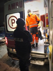 POLICJANTKA STOI PRZY KARETCE POGOTOWIA W ŚRODKU WIDAĆ RATOWNIKA MEDYCZNEGO
