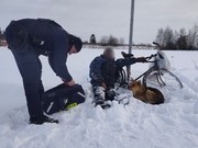 policjant i mężczyzna leżący w śniegu obok rower i pies
