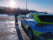 policjant stojący przy jezdni i radiowozie mierzący prędkość urządzeniem do mierzenia