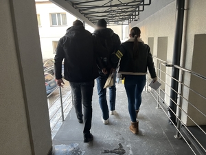 policjanci nieumundurowani idą z zatrzymanym w tle budynek