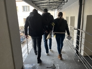 policjanci nieumundurowani idą z zatrzymanym w tle budynek