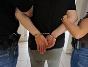 osoba w kajdankach zapiętych z tyłu na nadgarstkach prowadzona przez dwóch policjantów nieumudurowanych