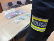 narkotyki na stole na pierwszym planie opaska z napisem policja na ramieniu policjanta