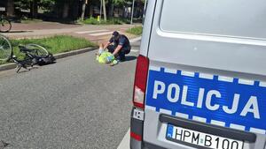 radiowóz w tle policjant udziela pomocy leżącemu mężczyźnie, rower wywrócony na poboczu