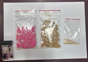 Zabezpieczone narkotyki, różowe i brązowe kapsułki oraz jasny proszek. Narkotester wskazujący metamfetamine.